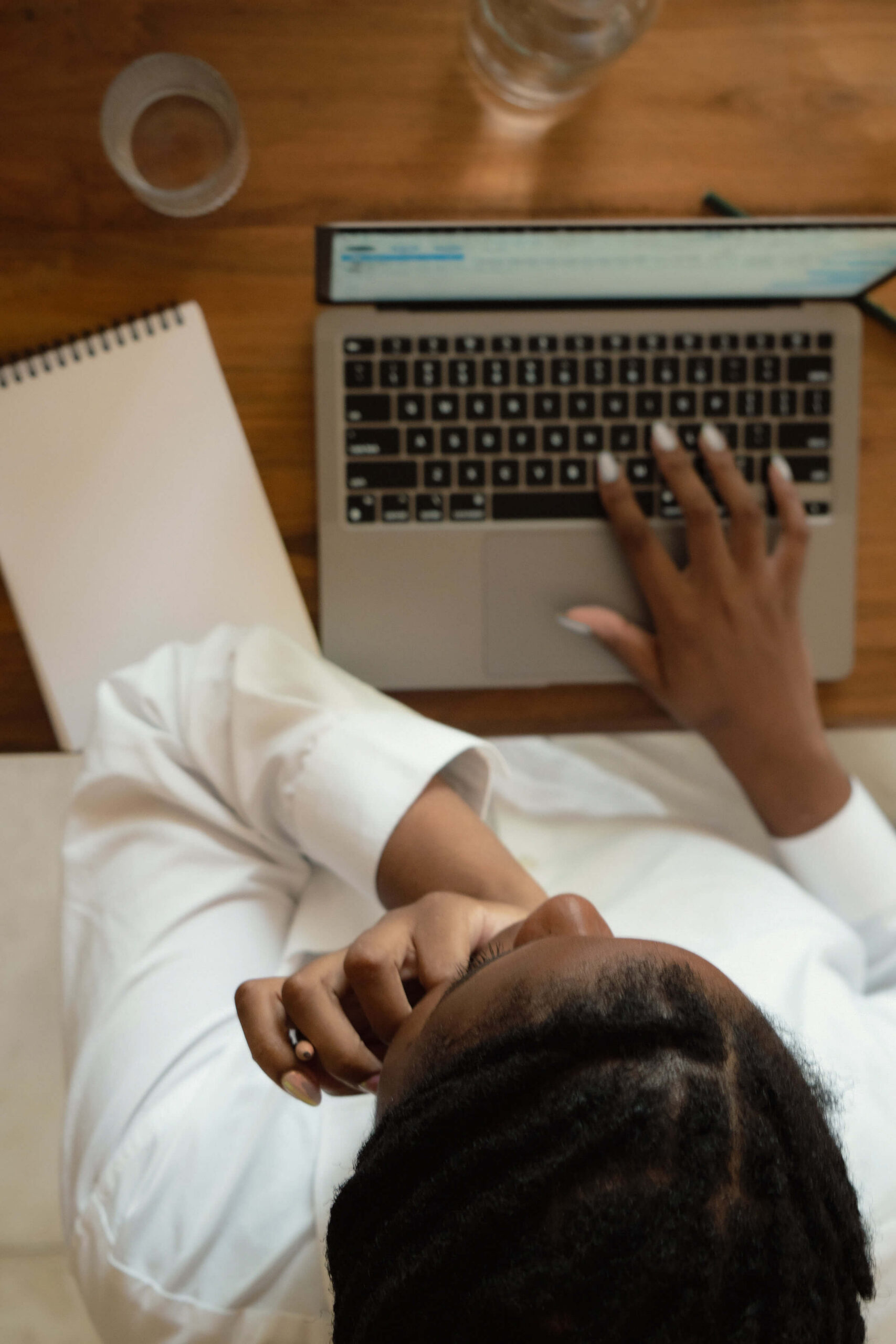Woman working on laptop with open notebook beside her